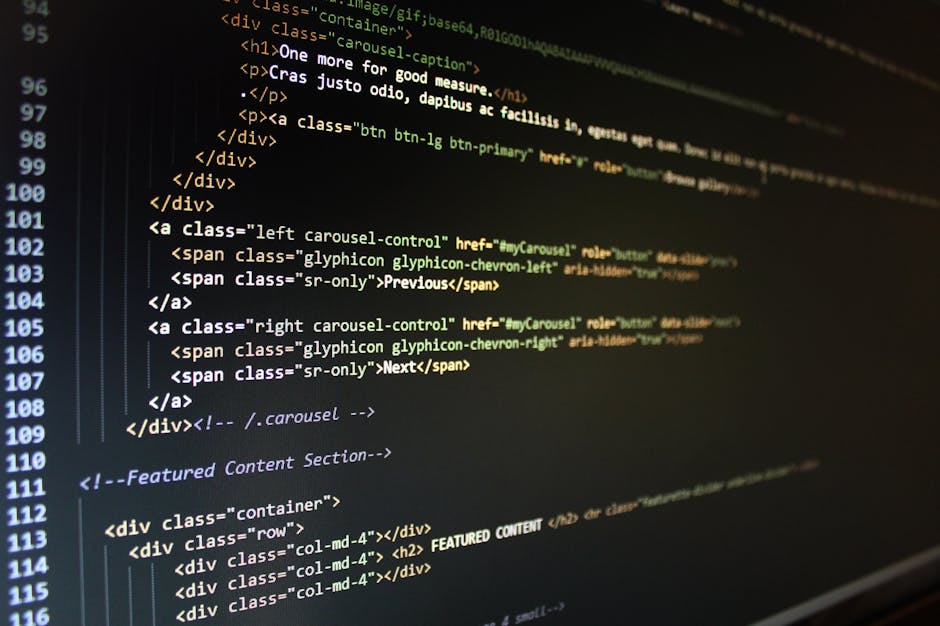 A person typing on a laptop placed on a dark, reflective surface. The laptop screen displays a code editor with lines of colorful programming code on a dark background. The person’s hands are visibl